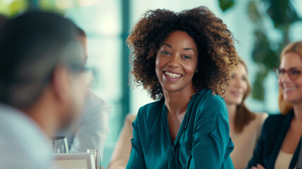 A smiling woman in a professional setting is engaged in a lively discussion with colleagues during a corporate meeting.