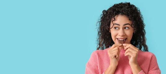 Canvas Print - Beautiful young African-American woman eating piece of sweet chocolate on light blue background with space for text