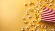 © Ilja - Delicious popcorn spilling from red striped box on pastel yellow background with space for text.