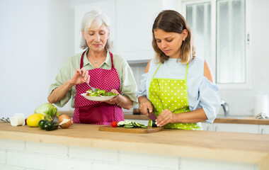 Wall Mural - Happy elderly woman and her adult daughter making dinner together in kitchen