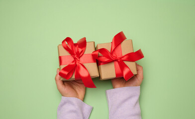 Wall Mural - Woman's hand holding a gift box wrapped in a red silk ribbon on a green background