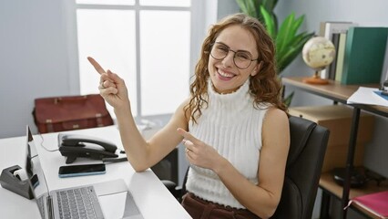 Sticker - Elegant young woman smiling cheerfully at camera while pointing to the side with both hands at office