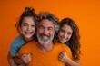 Father and two daughters smiling for the camera on orange background