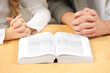 © New Africa - Girl and her godparent praying over Bible together at table indoors, closeup