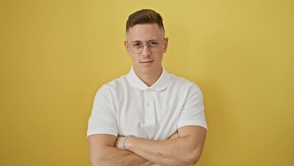 Sticker - Frowning young hispanic man wearing glasses, standing with arms crossed, expressing doubt and disapproval. negative emotion portrait against isolated yellow background.