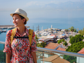 Wall Mural - female summer travel to Antalya, Turkey. young asian woman in red dress walk through old town Kalechi , Panoramic view of Antalya Old Town port, Taurus mountains and Mediterrranean Sea, Turkey