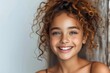 A portrait of a charming young girl smiling with naturally curly hair against a white background