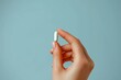 © LifeMedia - Skilfully framed, this image presents an individual's fingers gently presenting a single white pill, standing out against a calm pale blue background