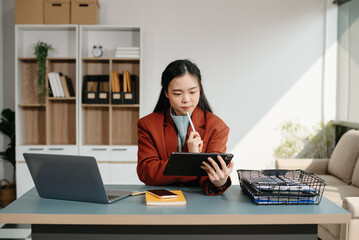 Asian businesswoman working with working notepad, tablet and laptop documents talking on the smartphone, tablet and laptop video call tax, report, accounting