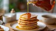  a stack of pancakes on a plate with syrup being drizzled on top of the pancakes and syrup being poured on top.