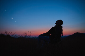 Wall Mural - man looking at the starry skies, crescent moon and planets in blue hour twilight time.