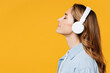 Leinwandbild Motiv Side profile view calm young woman she wearing blue shirt white t-shirt casual clothes listen to music in headphones close eyes isolated on plain yellow background studio portrait. Lifestyle concept.