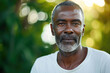 Headshot of senior African man with blurred nature background in morning sunlight. Elderly health and welfare services concept