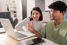 Young Couple Sharing A Fun Moment While Shopping Online, With The Woman Pointing At The Laptop Screen And Smiling