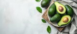 Top view of ripe avocados arranged on a white dish and wooden cutting board with cloth, creating a flat lay. Represents the concept of healthy fruits with space for text.