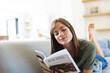© Wavebreak Media - A young Caucasian woman enjoys reading a magazine while relaxing on a sofa