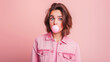 © XaMaps - A quirky portrait of a young woman in a pink denim jacket making a surprised face as a bubblegum bubble pops in front of a plain pink background