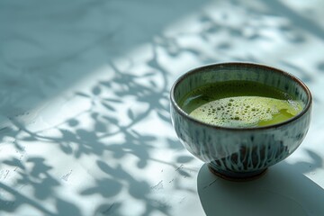 A cup of matcha green tea and matcha powder with a matcha green tea maker on a simple background.