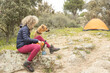 Curly and blonde hair, mountaineer woman and her dog camps and making tea with a gas stove