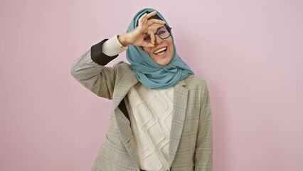 Poster - Happy middle age hispanic woman in hijab doing ok sign, looking through fingers with cheerful smile over pink isolated background