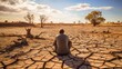 a man sits contemplatively looking at the cracked scorched earth soil drought desert landscape