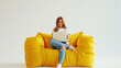 © Irina Sharnina - A beautiful young girl sits with a wireless laptop on a yellow chair on a white background.