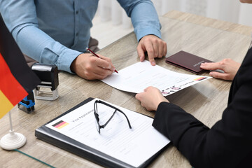 Wall Mural - Immigration to Germany. Man signing visa application form at wooden table, closeup