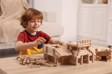 Wall Mural - Cute little boy playing with wooden construction set at table in room. Child's toy