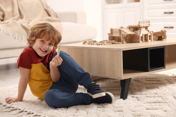 Poster - Cute little boy playing with wooden construction set on carpet at home. Child's toy