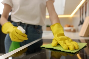 Wall Mural - Woman with spray bottle and microfiber cloth cleaning electric stove in kitchen, closeup