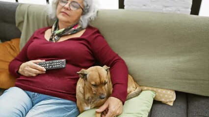 Canvas Print - Mature woman relaxing with pet dog on couch indoors while holding a remote.