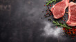 Raw beef steak on dark black board background, above top view, text copy space, uncooked raw beef steak,rosemary spices, cooking ingredients 