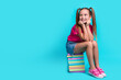 Full length photo of diligent schoolgirl wear t-shirt sit on book look at proposition empty space isolated on teal color background