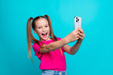 Poster - Portrait of cheerful positive little girl with tails dressed pink t-shirt make photo on smartphone isolated on turquoise color background