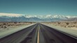 an empty road in the middle of the desert with a mountain range in the distance with snow on the top of the mountains.