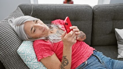 Poster - Middle age grey-haired woman using smartphone lying on sofa at home