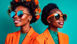A couple of very pretty young African American women dressed in orange clothes and sunglasses isolated on a teal background