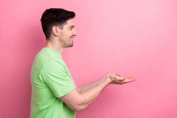 Poster - Side profile photo of young happy smiling funny man holding two hands promote new product advert isolated on pink color background