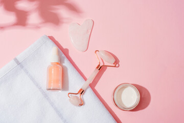 Wall Mural - Cosmetic serum bottle, cream jar and face roller, gua sha stone on pink background with plant shadows. Skin care, spa and wellness concept. Top view, flat lay