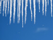 Many long crystal icicles with fall down drops hangs down close-up against clear cloudless blue sky in spring day