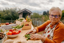 Elderly Woman Sorting Vegetables At A Rustic Table