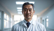 Confident Old Japanese Male Doctor or Nurse in Clinic Outfit Standing in Modern White Hospital, Looking at Camera - Professional Medical Portrait, Copy Space, Design Template, Healthcare Concept