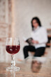 A glass of red wine takes center stage, with a woman reading a book in the background, creating a sense of both relaxation and intrigue.