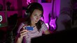 Focused woman wearing headphones holds credit card in neon-lit gaming room at night.