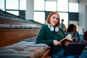 Wall Mural - Smiling female student learning in lecture hall and looking at camera.