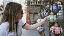 A brunette woman smiles while exploring the traditional lanterns at souq waqif in doha, wearing casual attire.