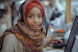 © Raptecstudio - A woman with a hijab and headphones is smiling while using a laptop