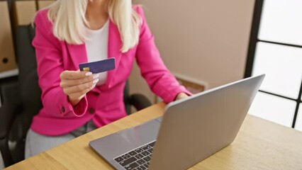 Canvas Print - Successful young blonde businesswoman confidently manages finances, smiling as she works online with laptop and credit card in the office