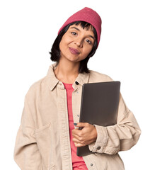 Wall Mural - Cheerful young Hispanic student with laptop and beanie in studio