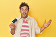 © Asier - Man holding credit card on yellow receiving a pleasant surprise, excited and raising hands.